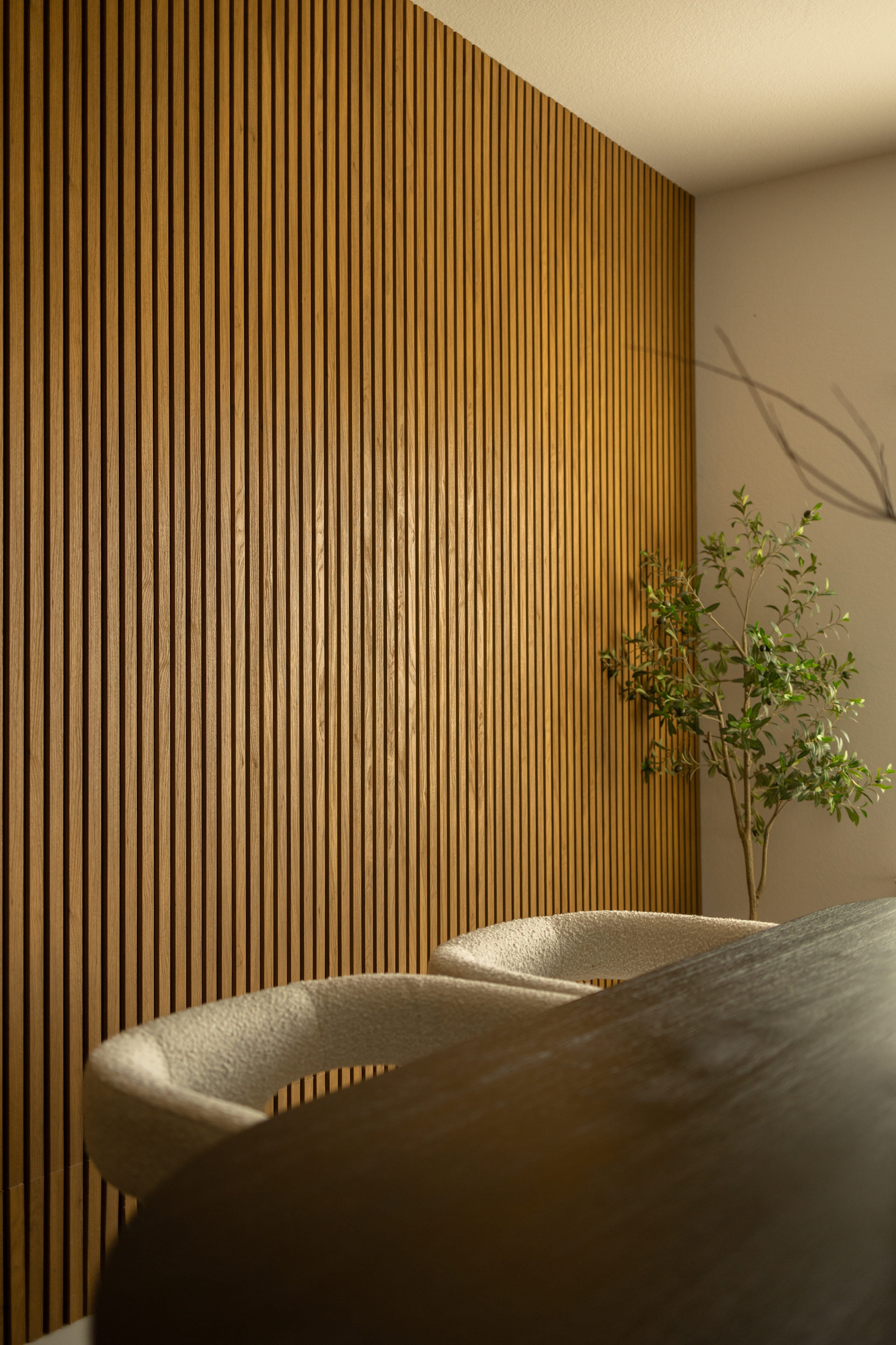 Akupanel acoustic wood slat wall panels in a softly lit interior with chair and potted plant visible.